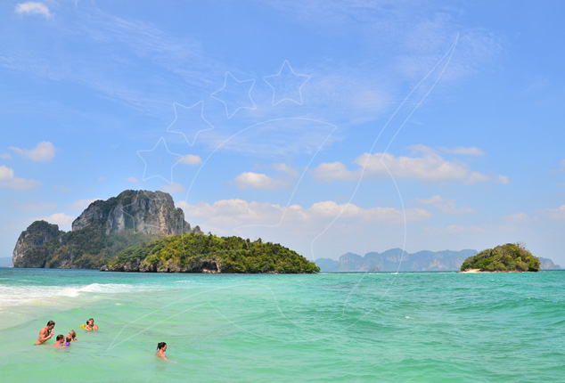 Swimmers in turquoise shallows off a Thai beach with limestone karst islands under a blue sky