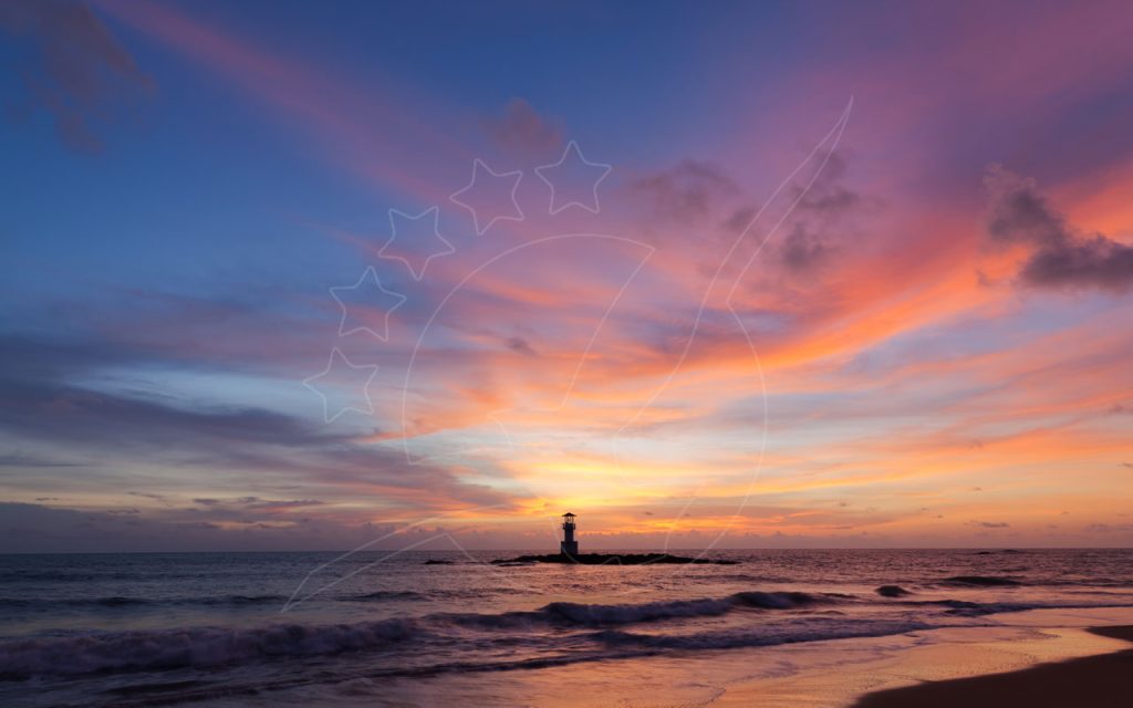 Faro in controluce su frangiflutti roccioso al tramonto, cielo rosa e arancio sopra onde su spiaggia sabbiosa