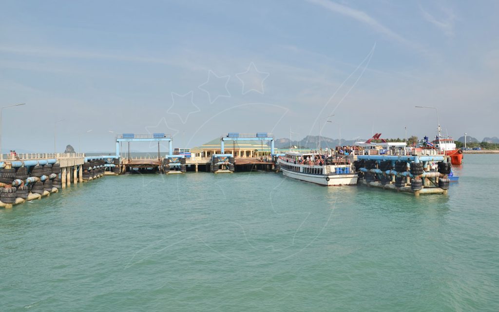 Passenger ferry boarding at a concrete pier with tyre fenders on calm turquoise sea, karst hills on the horizon