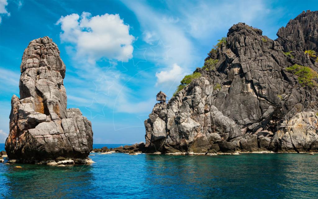 เขาหินปูนสูงชะลูดและเกาะหินขรุขระที่มีกระท่อมหลังเล็ก ผุดขึ้นจากน้ำสีเทอร์ควอยซ์ใต้ฟ้าสีคราม