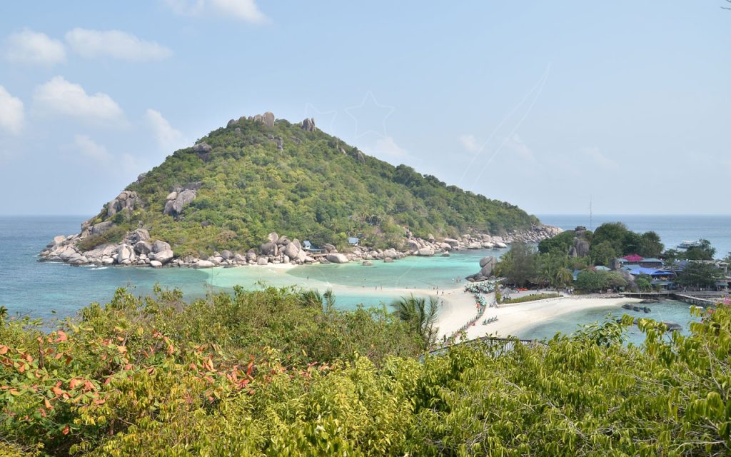 สันทรายเชื่อมเกาะหินแกรนิตปกคลุมป่า น้ำตื้นสีเทอร์ควอยซ์ ร่มชายหาดและท่าเรือที่เกาะนางยวน ประเทศไทย