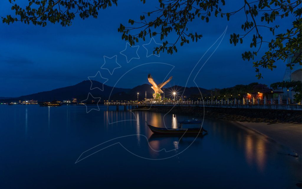 蓝调时刻兰卡威老鹰广场上灯光照亮的雄鹰雕像,平静海湾中停着木船