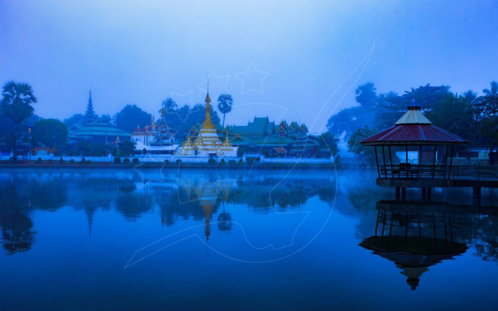 ブルーアワーに霧の湖に映る金色のタイ寺院と東屋、メーホンソーン風の湖畔の町の風景