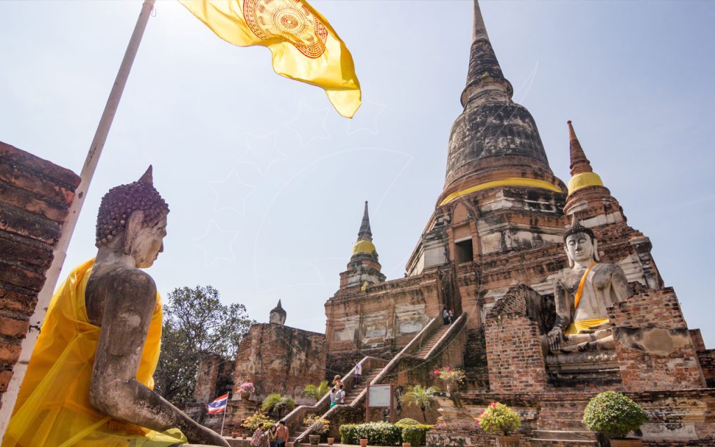 Statue di Buddha seduti con fasce gialle davanti a un grande stupa di mattoni e a una bandiera gialla in un tempio in stile Ayutthaya, Thailandia