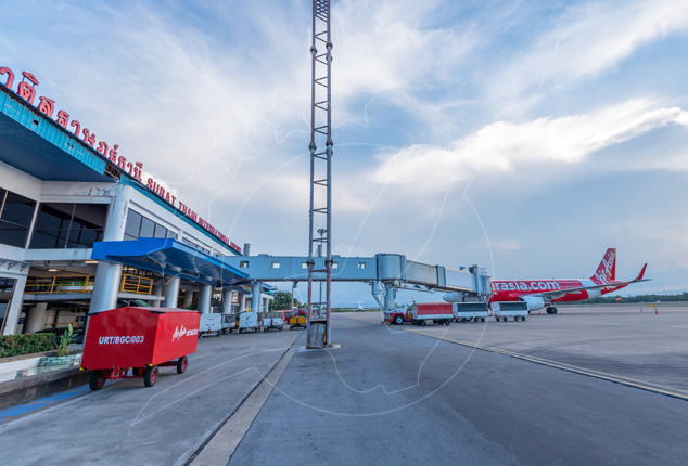 AirAsia aircraft parked at Surat Thani Airport terminal with jet bridge and red baggage carts on the apron