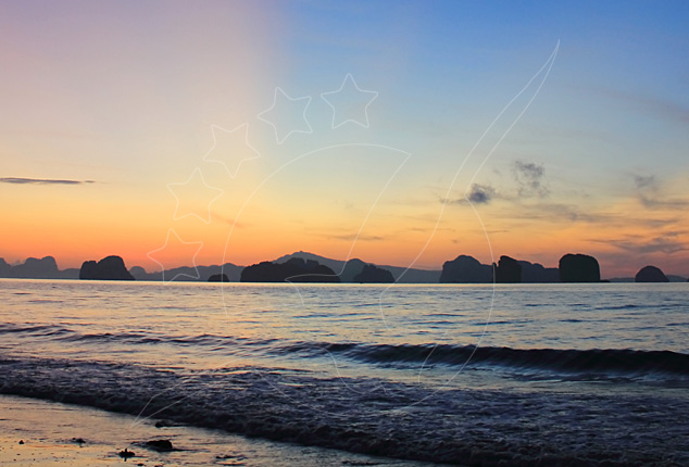 Sunset over calm sea with limestone karst islands silhouetted on the horizon and small waves rolling to shore