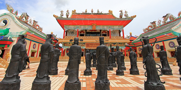 Rows of dark bronze Chinese sage statues in a tiled courtyard before an ornate red-roofed Chinese temple hall under blue sky