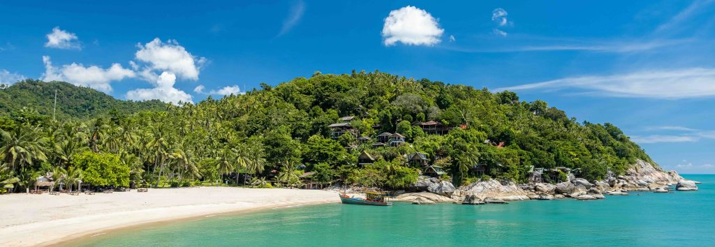 Baia tropicale con scogliere calcaree, giungla rigogliosa, barca tradizionale di legno e acqua turchese sotto cielo azzurro