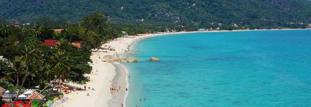 Baia turchese con spiaggia di sabbia bianca, palme ed edifici residenziali sulla collina