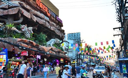 Tourists and traffic on Bangla Road, Patong, past a rock-facade nightlife complex with tiger statues and colourful flags